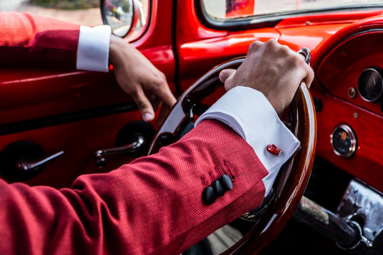 A man in a red suit driving a vintage car with a wooden steering wheel.